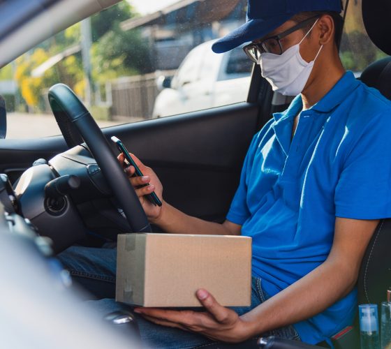 Asian delivery man courier online holding deliveries out boxes in car and using mobile phone contact the customer he protective face mask service under curfew quarantine pandemic coronavirus COVID-19