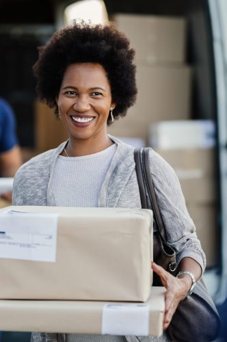 Happy African American woman holding delivered packages. A couriers is standing in the background.